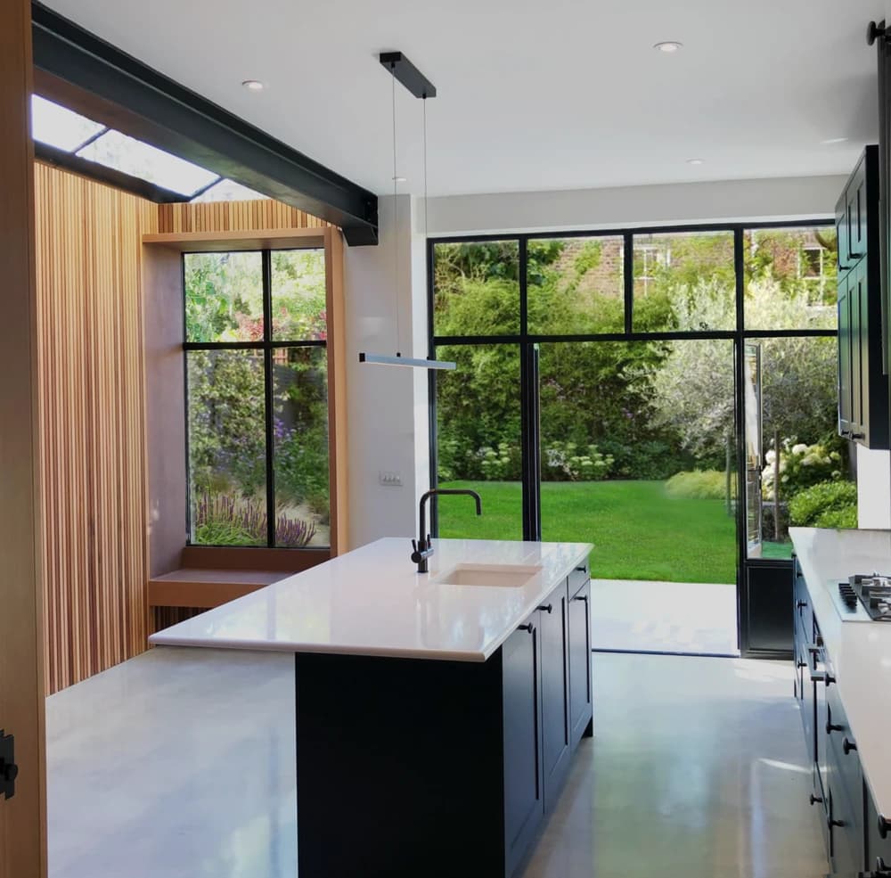 Kitchen extension in Hornsey N8 with an exposed steel beam beside roof glazing, timber slats and a window seat next to the island