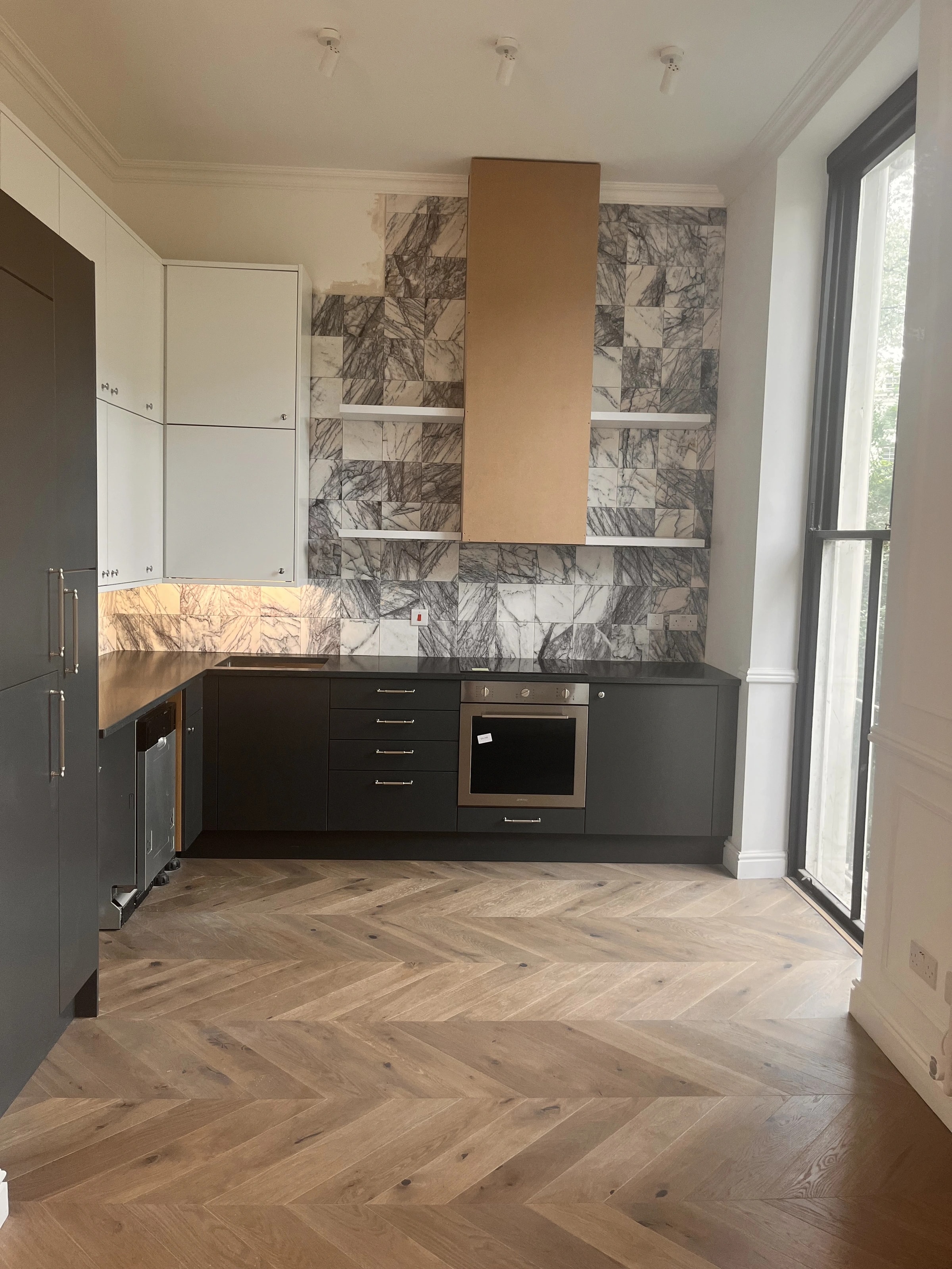 Kitchen with dark cabinetry, veined splashback and herringbone flooring