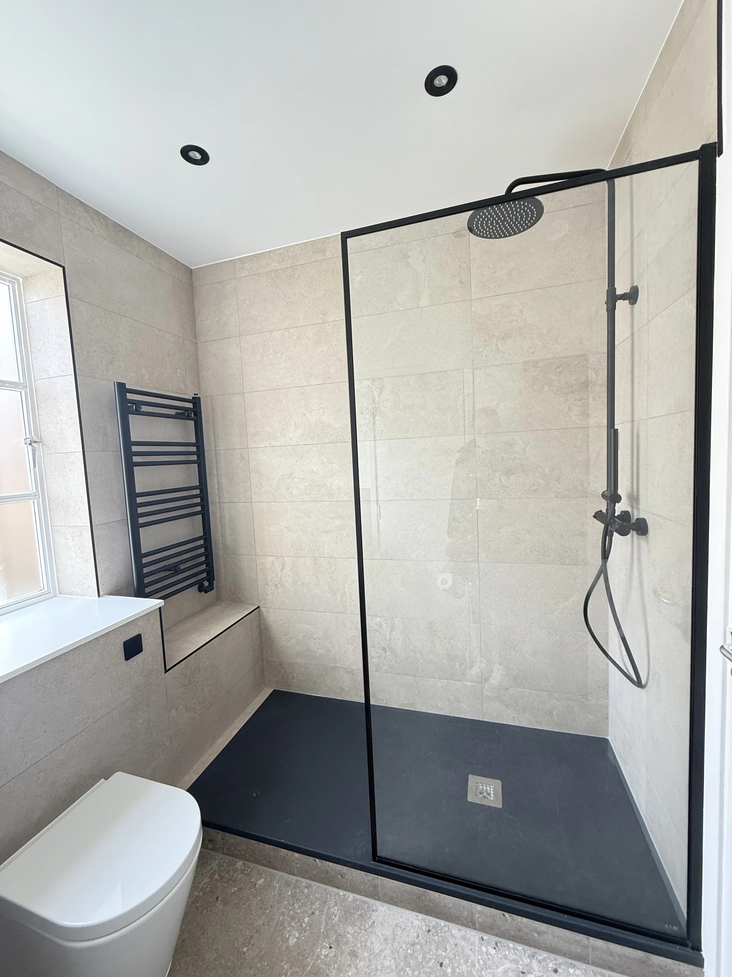 Walk-in shower with black-framed glass and pale wall tiles